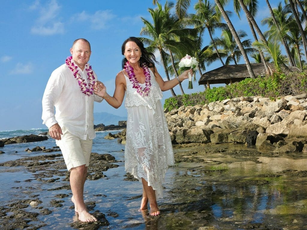 Just-married couple holding hands walking on rocks at shore