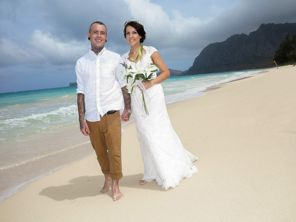Couple holding hands in wedding attire walking on beach